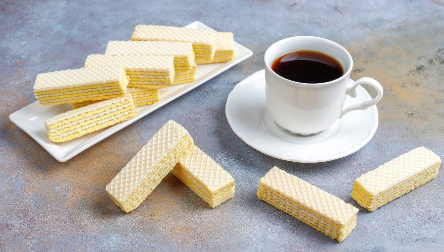 Tanko sečene oblande, nalik na napolitanke poređane na pravougaonoj tacni i stolu pored šoljice kafe.