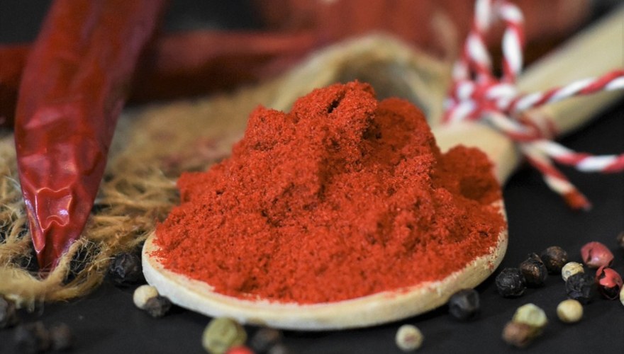 Mlevena crvena paprika pored suve crvene paprike.